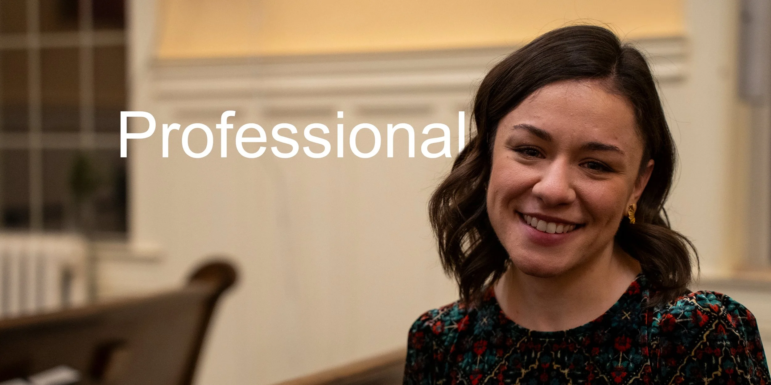 A woman with dark brown hair and a patterned dress smiling indoors.