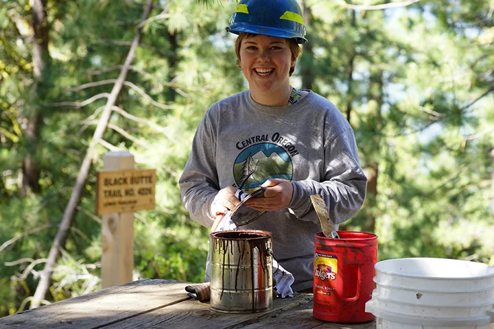 Scout Miller mixes paint for a fresh coat being applied on the information kiosk. She is part of a team of Youth Conservation Corps young adults led by 2nd generation USFS employee Rikki Glick that was working to restore trailhead facilities at the beginning of the Black Butte FIre Lookout trail. The YCC has introduced young Americans to conservation opportunities in public lands since the program was created in 1970. Photo by Gary Miller