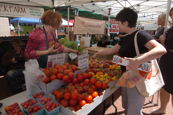 A shopper picks out tomatoes at a Farmer's market in Portland. Photo by Mary Volm
