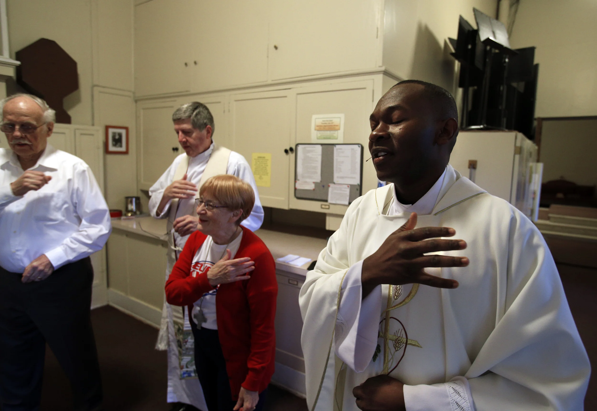 6:51 a.m. Father Chrispine Otieno, right, makes the sign of the cross as he prays before the morning Mass on Monday, July 15, 2013. He is shown in the sacristy of St. Mary Catholic Church in downtown Eugene with parishioners and Father Dan Maurer. St. Mary Parish was established in 1887 in Eugene; the present church was built in 1927. (Paul Carter/The Register-Guard)