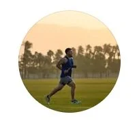 A person running on a grassy field during sunset with trees in the background.