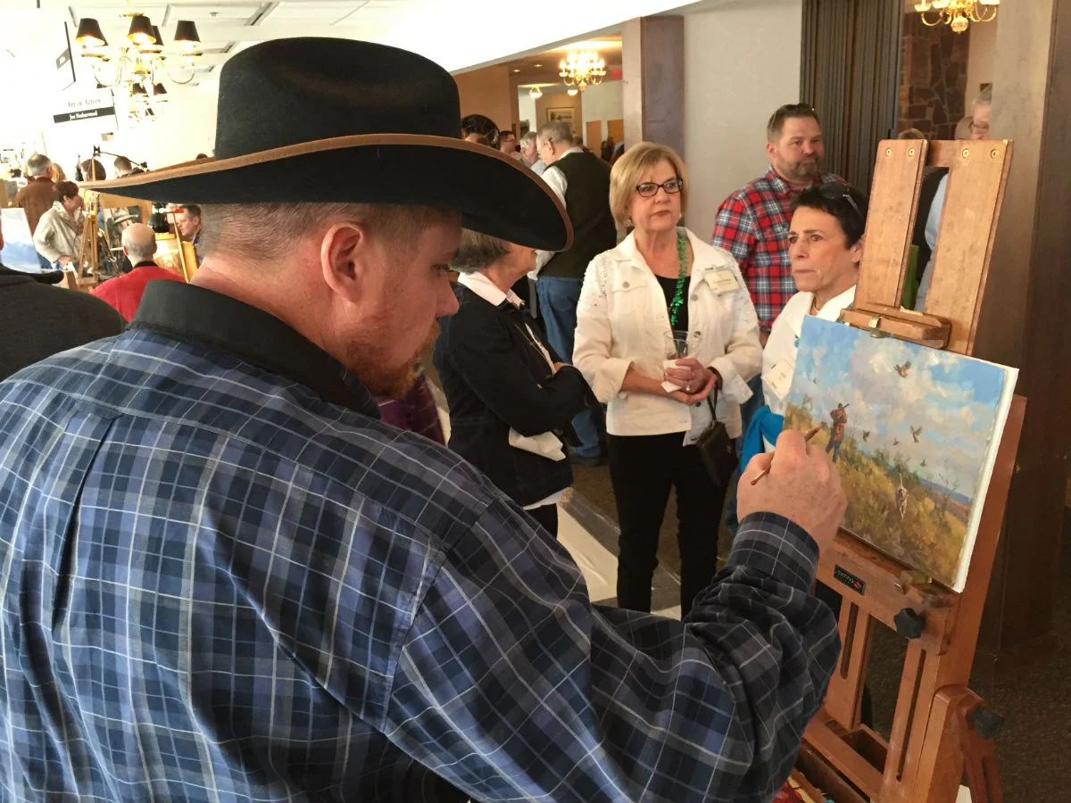 Artist Chad Poppleton finishes a painting to be auctioned while interested buyers eagerly watch.