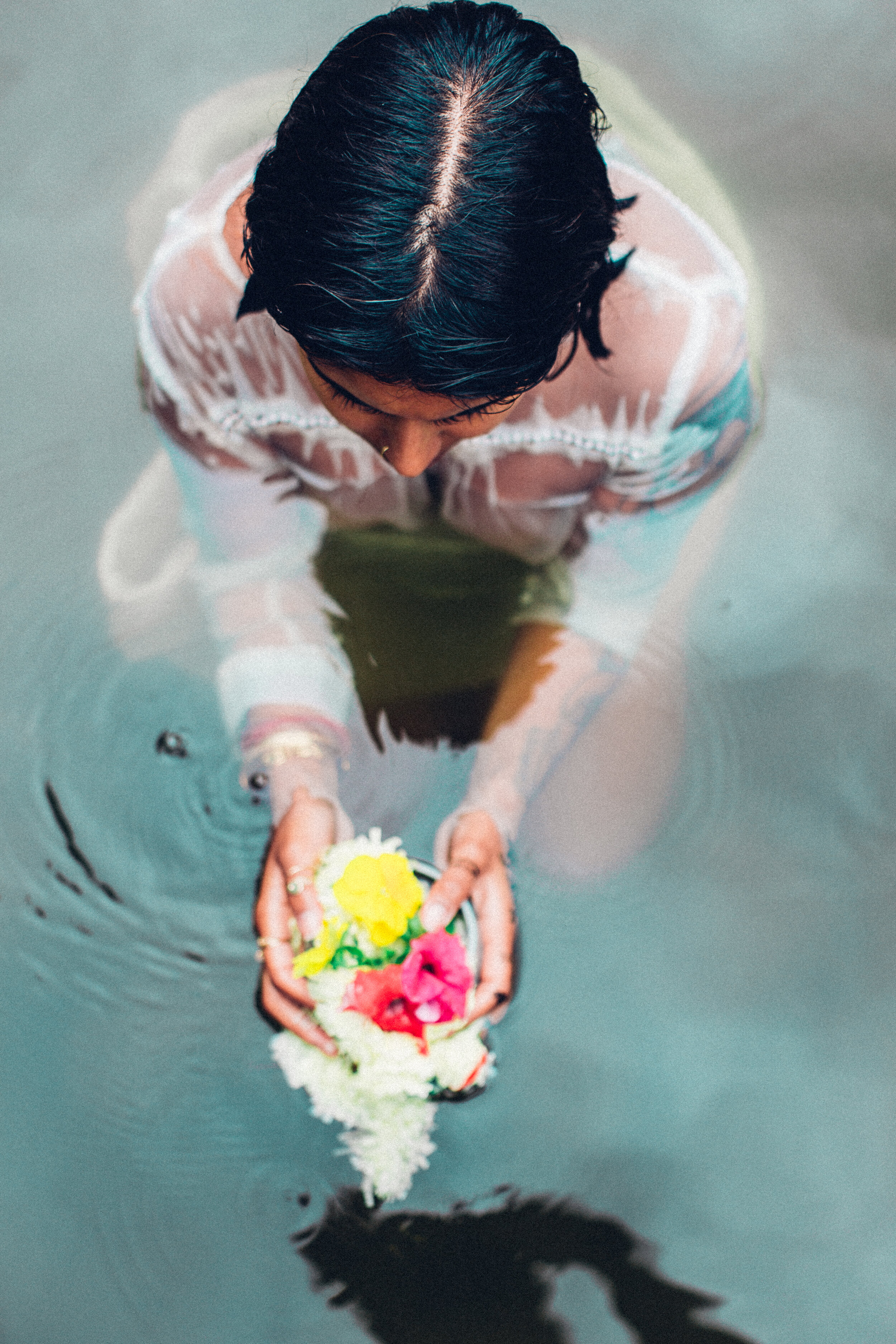  Image description: Angle above a woman sitting in water holding flowers.  