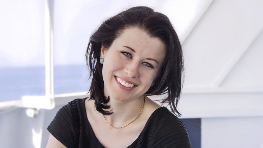 Molly Suber Thorpe’s headshot, smiling, dark hair, wearing a black top and earrings, on a boat with the ocean in the background.