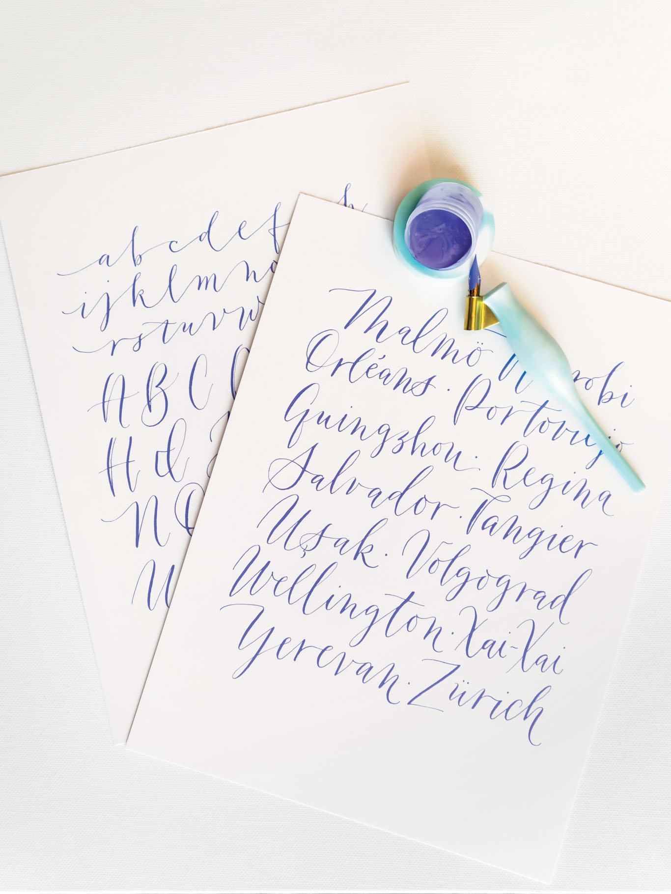 Close-up of modern calligraphy writing in purple gouache ink with turquoise pointed calligraphy pen and matching ink well