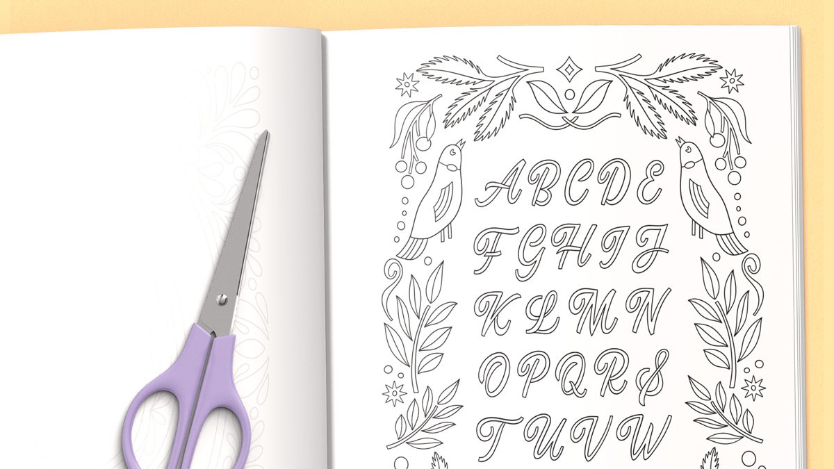 Decorate Alphabets Coloring book open spread with purple scissors laid on top to illustrate that pages can easily be cut out