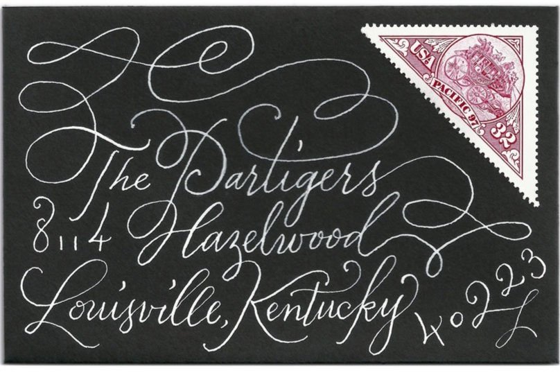 Black envelope with white flourished calligraphy handwriting and a red 32-cent triangular USA postage stamp in the top right corner.