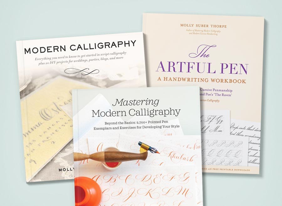Three of Molly Suber Thorpe’s calligraphy books stacked on a light blue surface: Modern Calligraphy, Mastering Modern Calligraphy, and The Artful Pen.