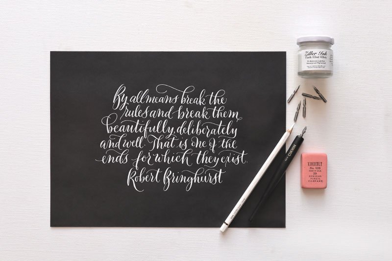 A quote by Robert Bringhurst in white ink modern calligraphy on black paper, with the calligraphy supplies used appearing next to the paper
