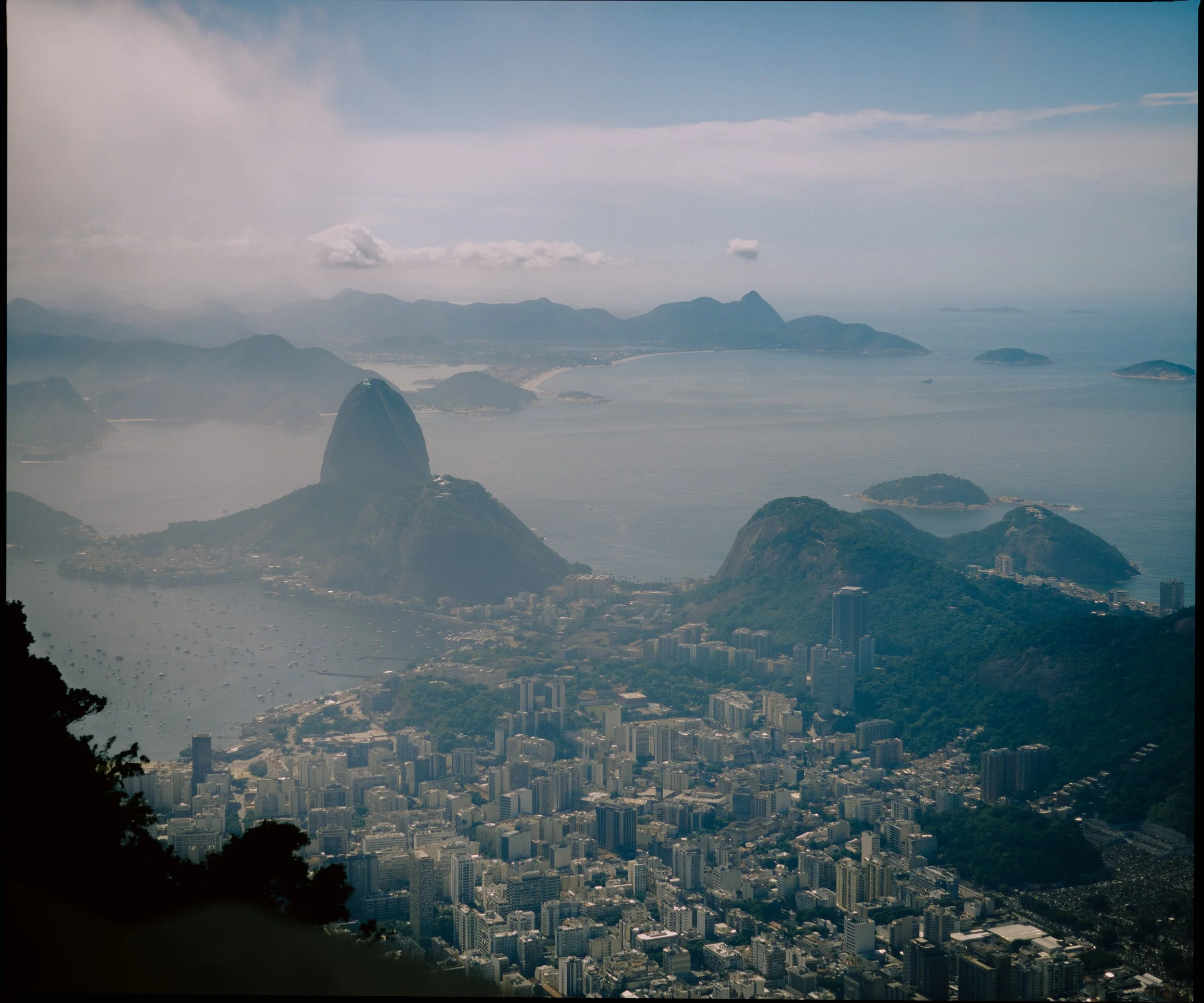 Aerial view of a city with mountains in the background, featuring tall buildings and the coastline in the distance.