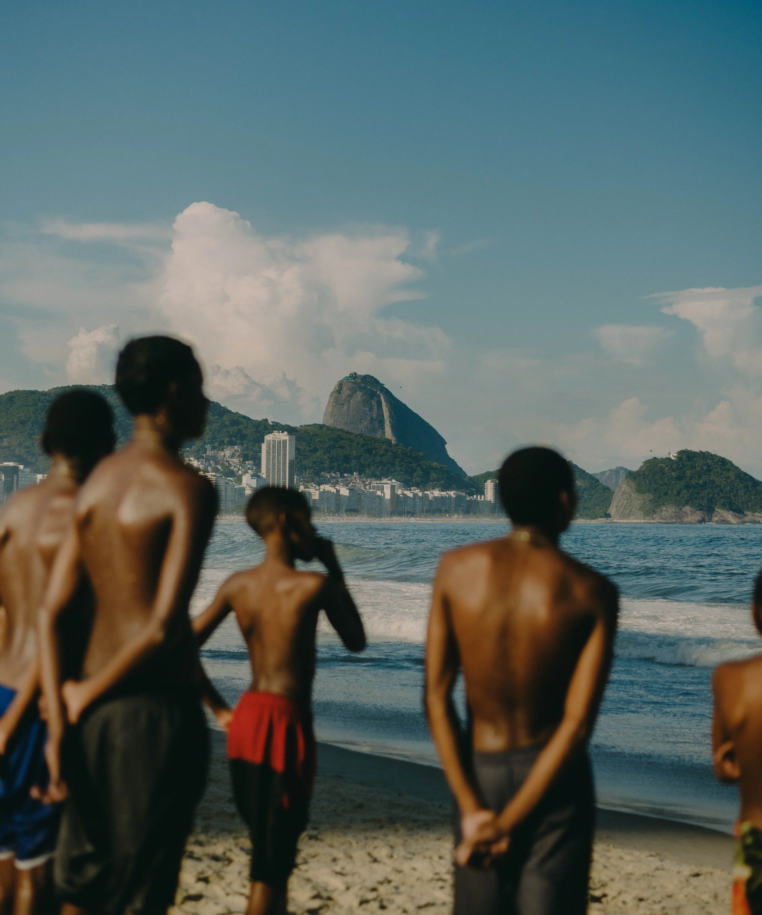 People at the beach with Mount Sugarloaf in the background under a blue sky with clouds.