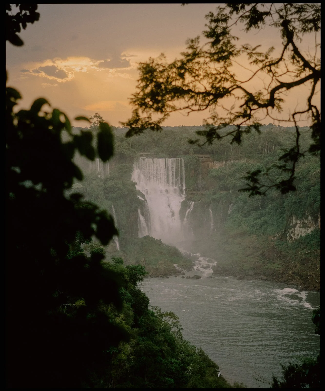 Sunset view of waterfalls through trees over a river.