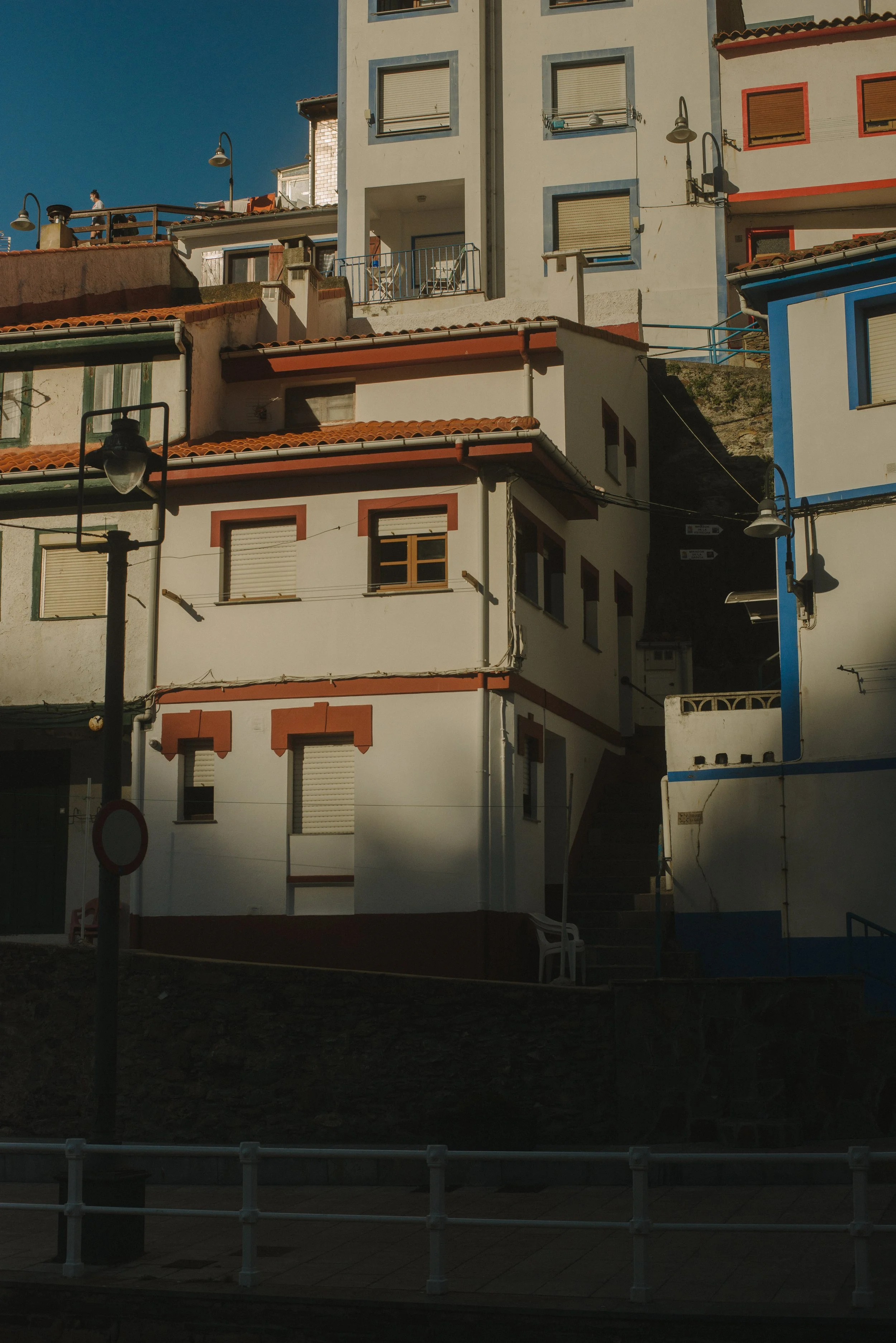 A multicolored residential building with multiple balconies, windows with closed shutters, and exterior lighting, under a clear blue sky.