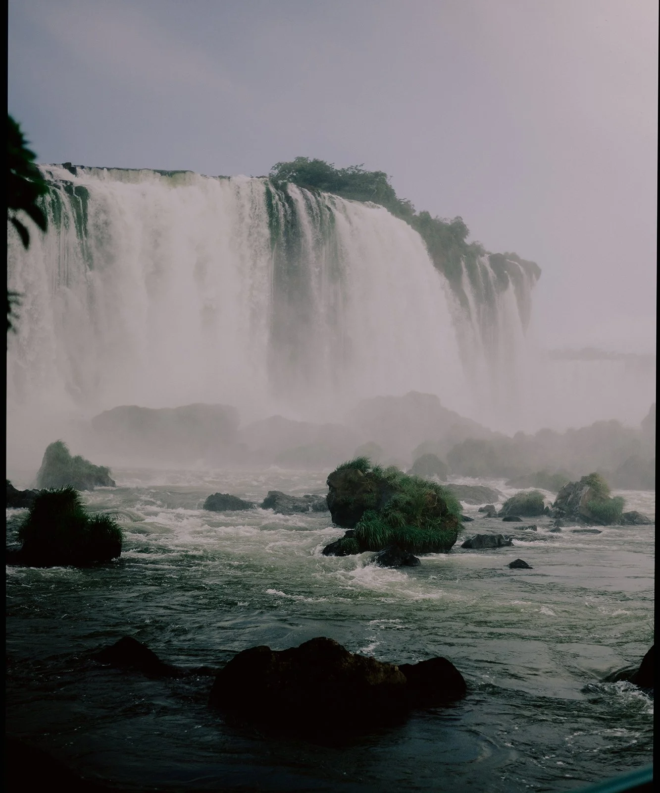 Photo of a large waterfall with mist rising, surrounded by rocks and greenery at the base.