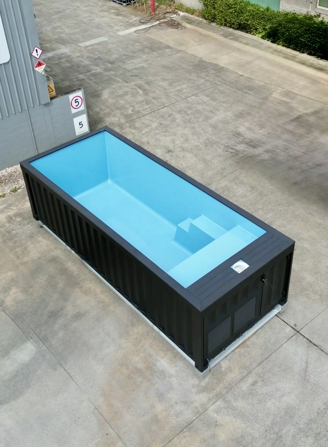 A large above-ground rectangular swimming pool with a black exterior and blue interior, situated outdoors on a concrete surface.