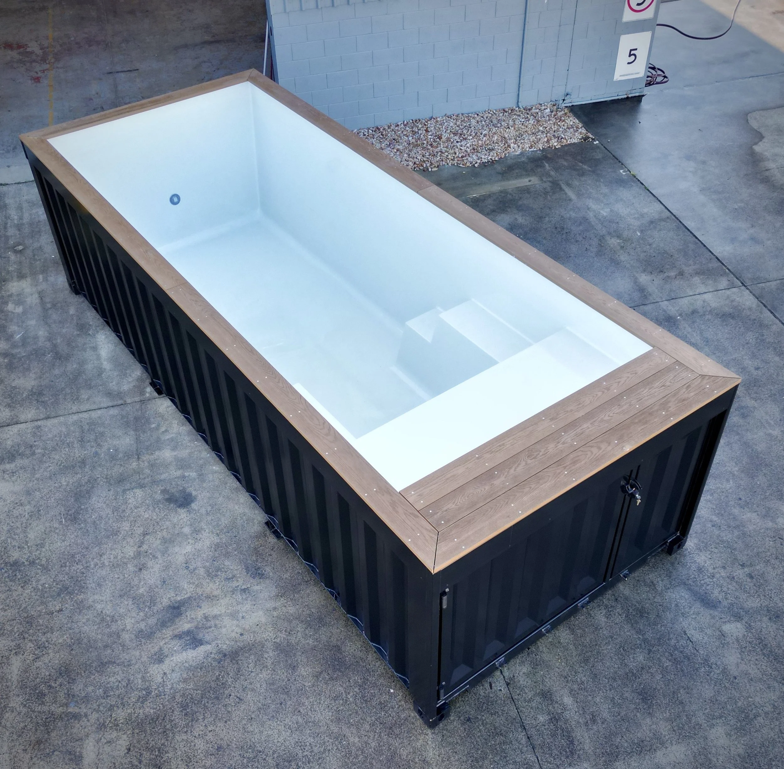 Empty rectangular hot tub with a white interior and wooden rim, situated outdoors on a concrete surface.