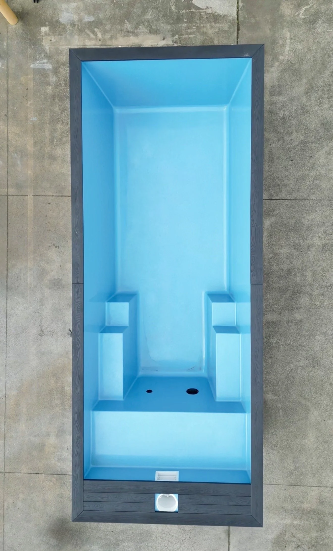 Blue and gray outdoor pub table with built-in cooler and drainage, seen from above on a concrete surface.