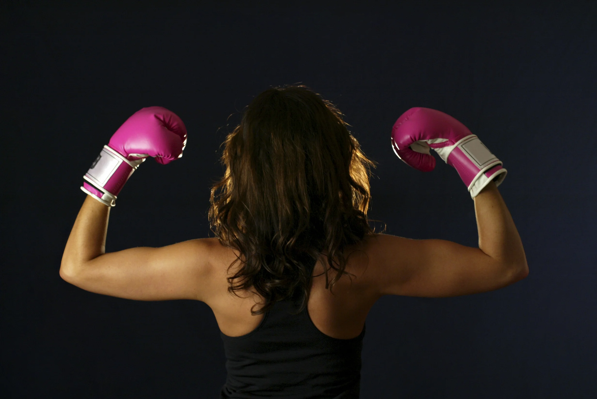 flexing.biceps.pinkboxinggloves.woman.youngadult.exercise.blackbackground.jpg