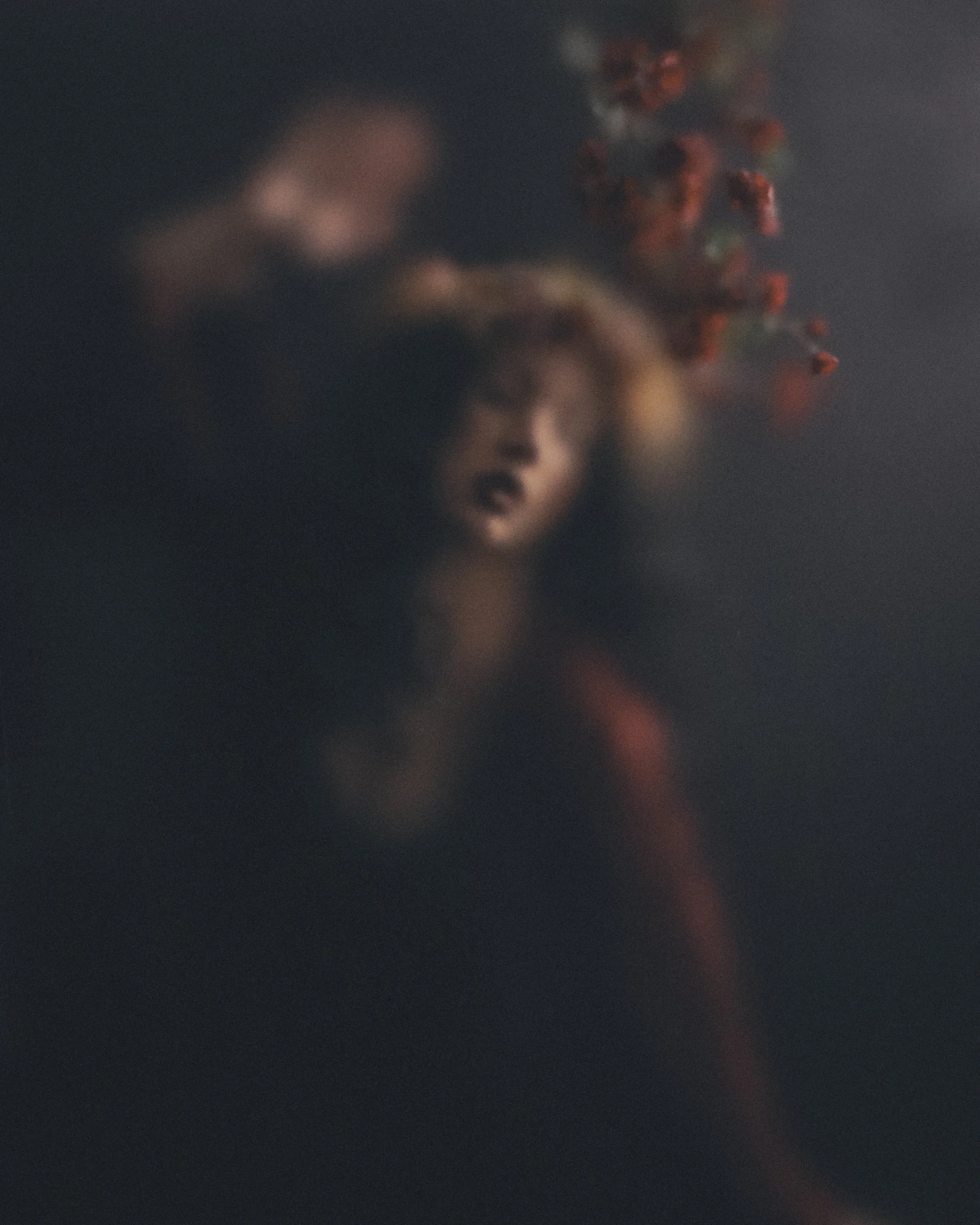 self portrait photo of Kalliope Amorphous in red with red flowers hanging overhead
