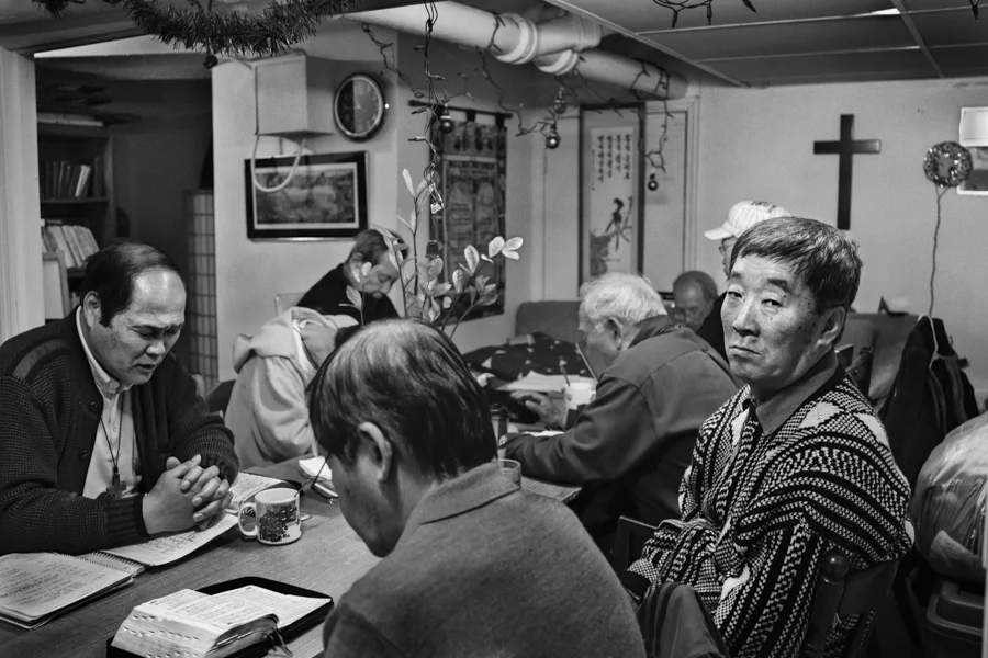Moses Chon, left, prays during a service held at the temporary shelter, Love Mission House, in Flushing, United States. Chun Hae-Young, a regular casino day-tripper, observes, but does not participate in in the prayer service, Feb. 28, 2013. Moses urges the homeless to participate in the services that are held daily at the shelter.