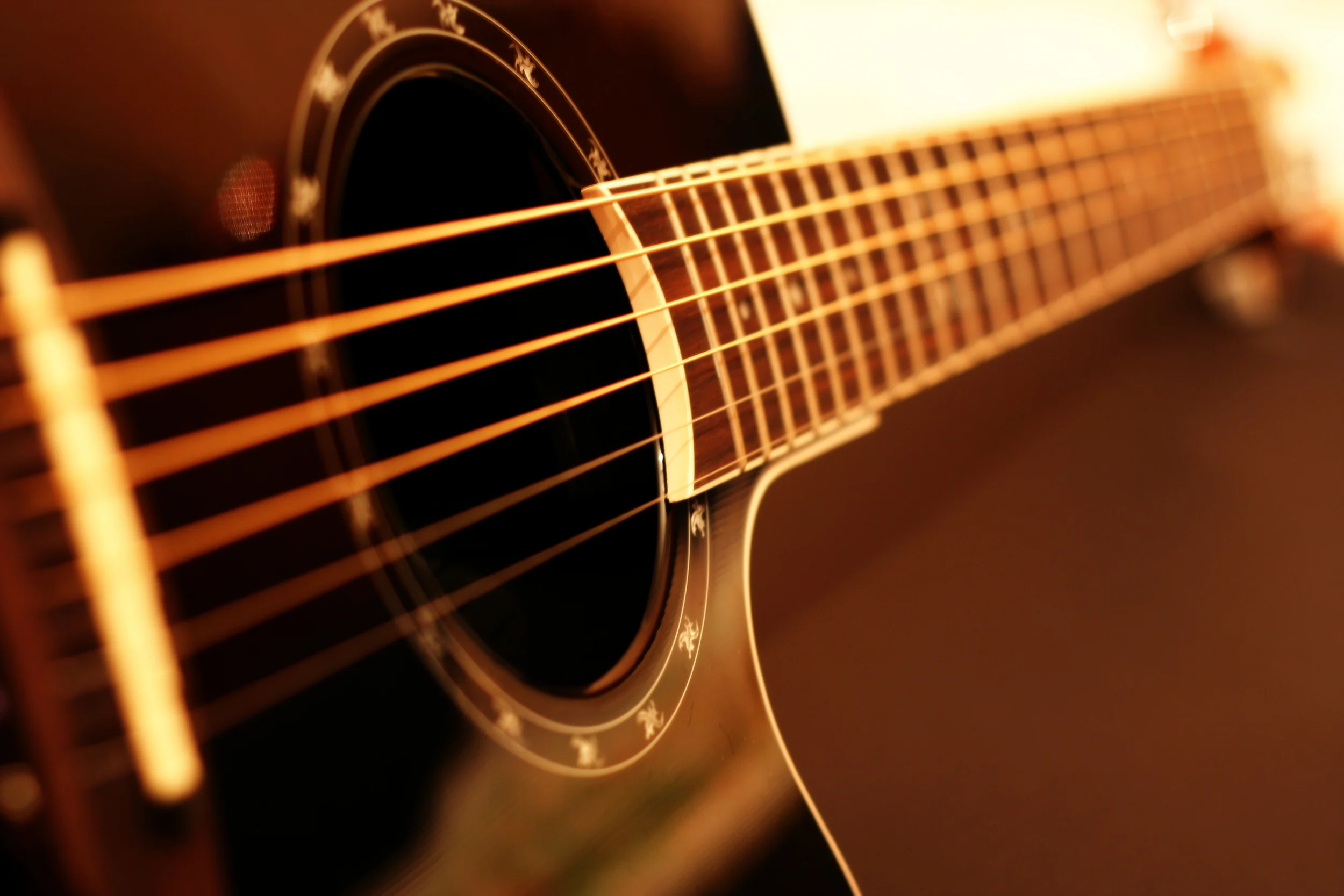 Close-up of an acoustic guitar with focus on the sound hole and strings, illuminated with warm light.