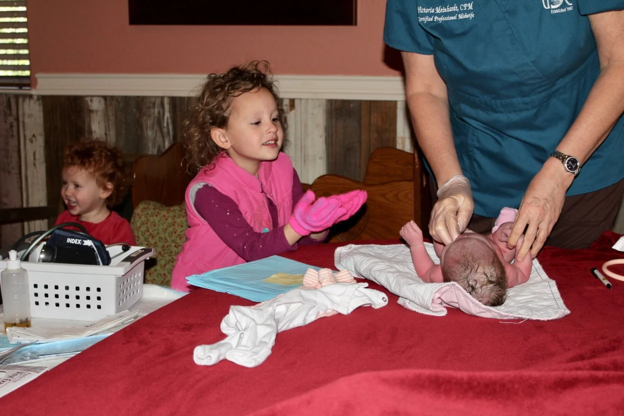 That first-born baby looking on while the fourth-born is getting vitals checked. Olivia, number three, is the photo bomber. 