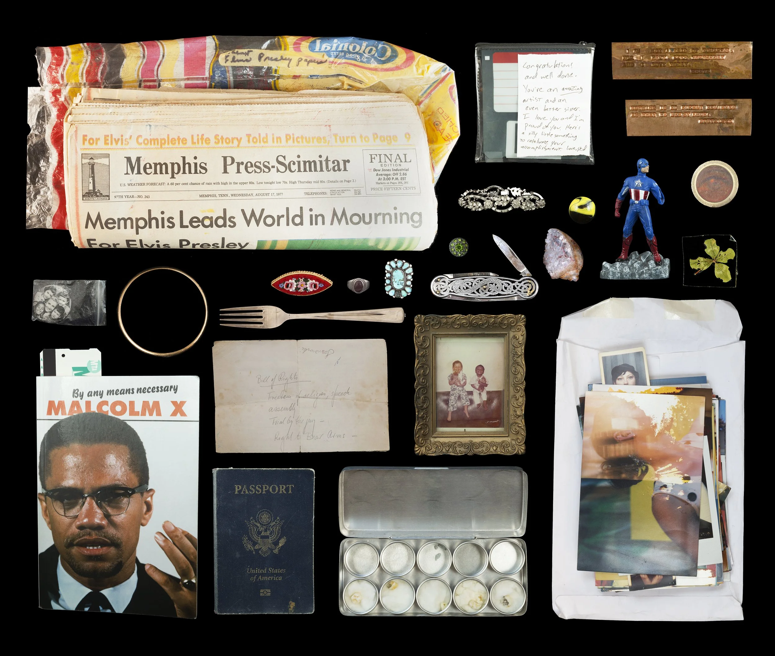 Collection of assorted personal items including a newspaper, a Malcolm X pamphlet, a passport, jewelry, a photograph, a toy Captain America figure, a small container of painted rocks, a vintage photograph frame, a collection of photographs in a white