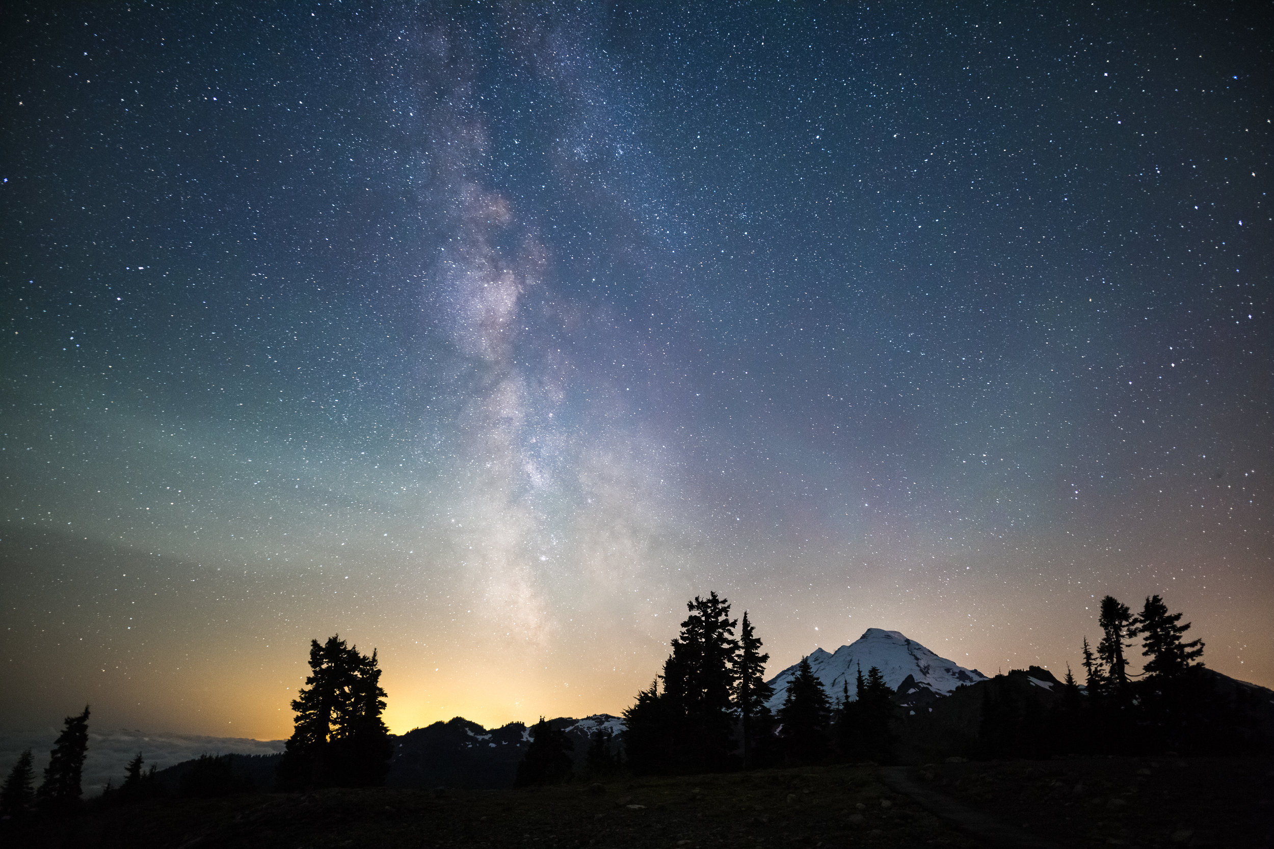  The distant Mount Baker towers over the landscape as the Milky Way streaks across the sky. The distant city lights of the greater Seattle area glow on the horizon.&nbsp; 