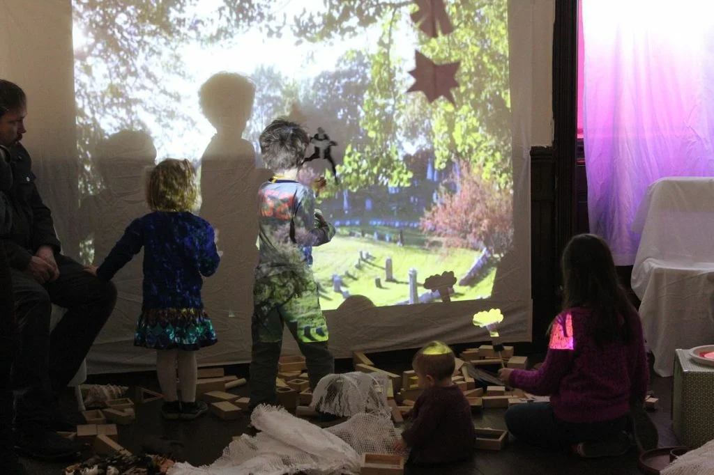 Children build with blocks and play with shadow puppets, in a space enhanced by a video projection on the wall.