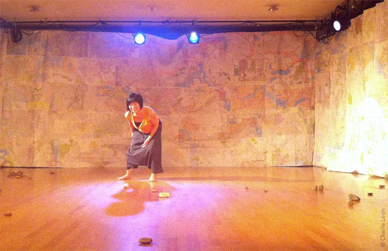 Performer Tomoko Hiraoka performing in Homing Devices. Set is constructed out of AAA maps sewn together to create full-scale fabric.