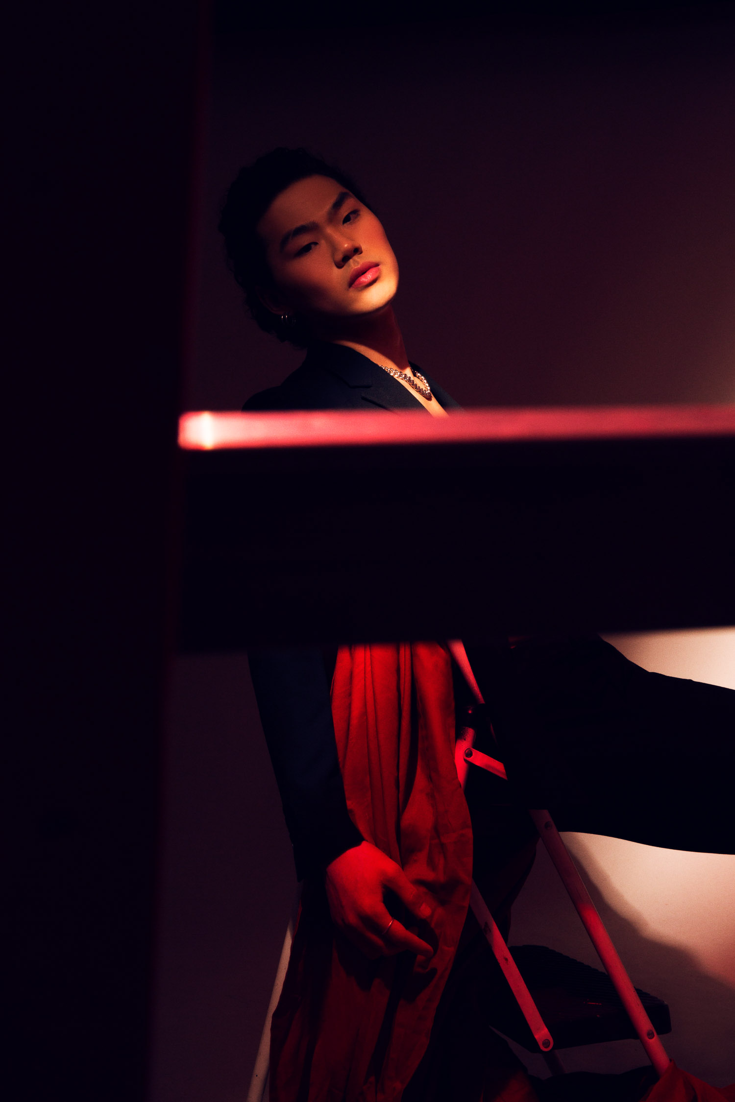 Asian man in red and black sitting on a metal stool.