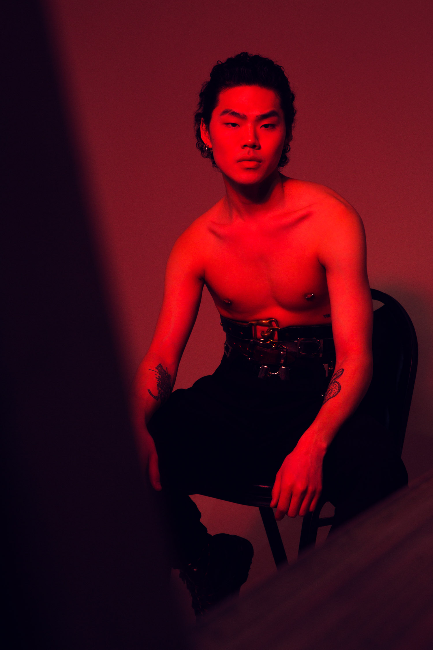 Shirtless man in red light sitting on a chair.