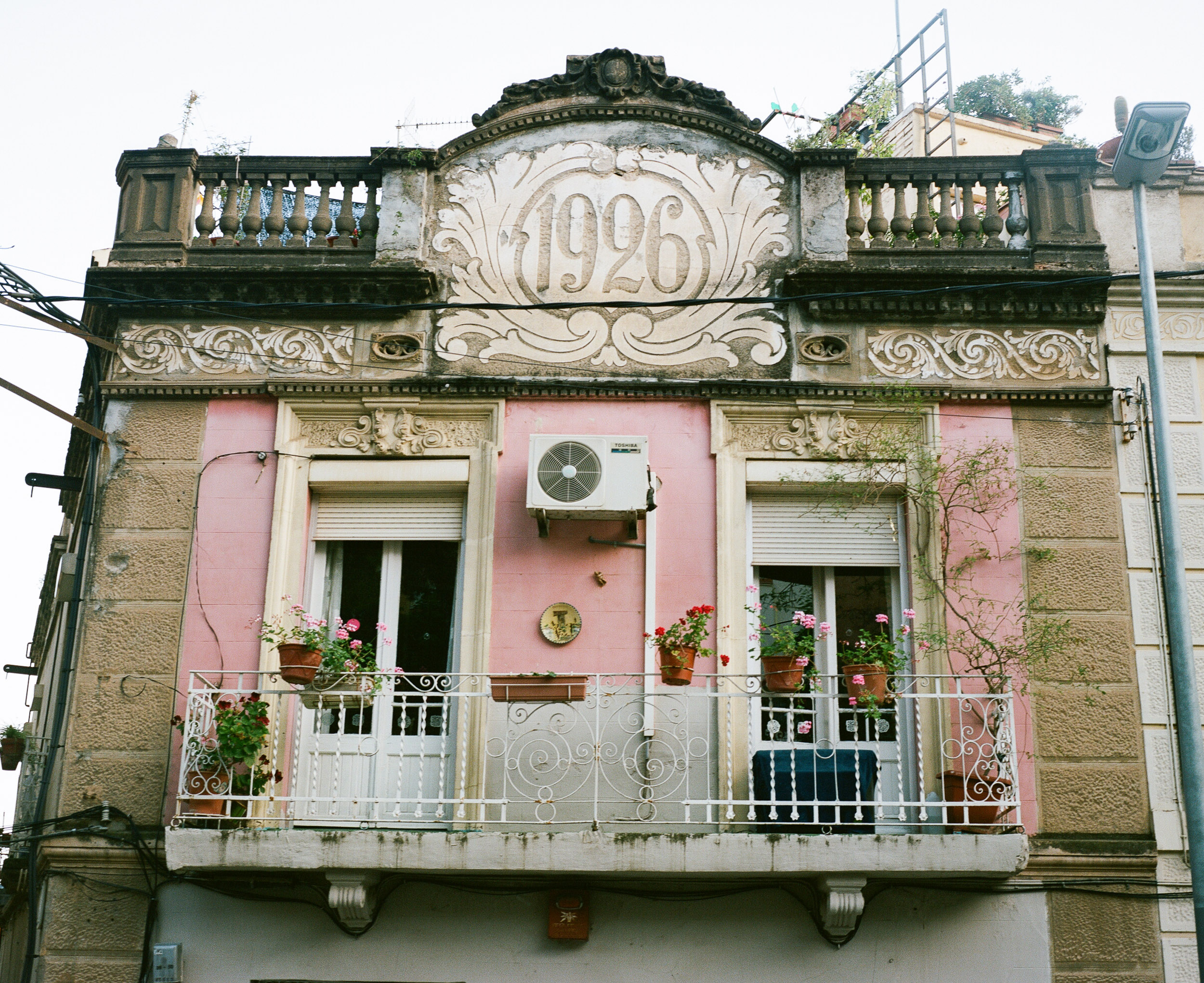 Pink house with balcony and an airconditioner, numbered 1926, in Barcelona, Spain