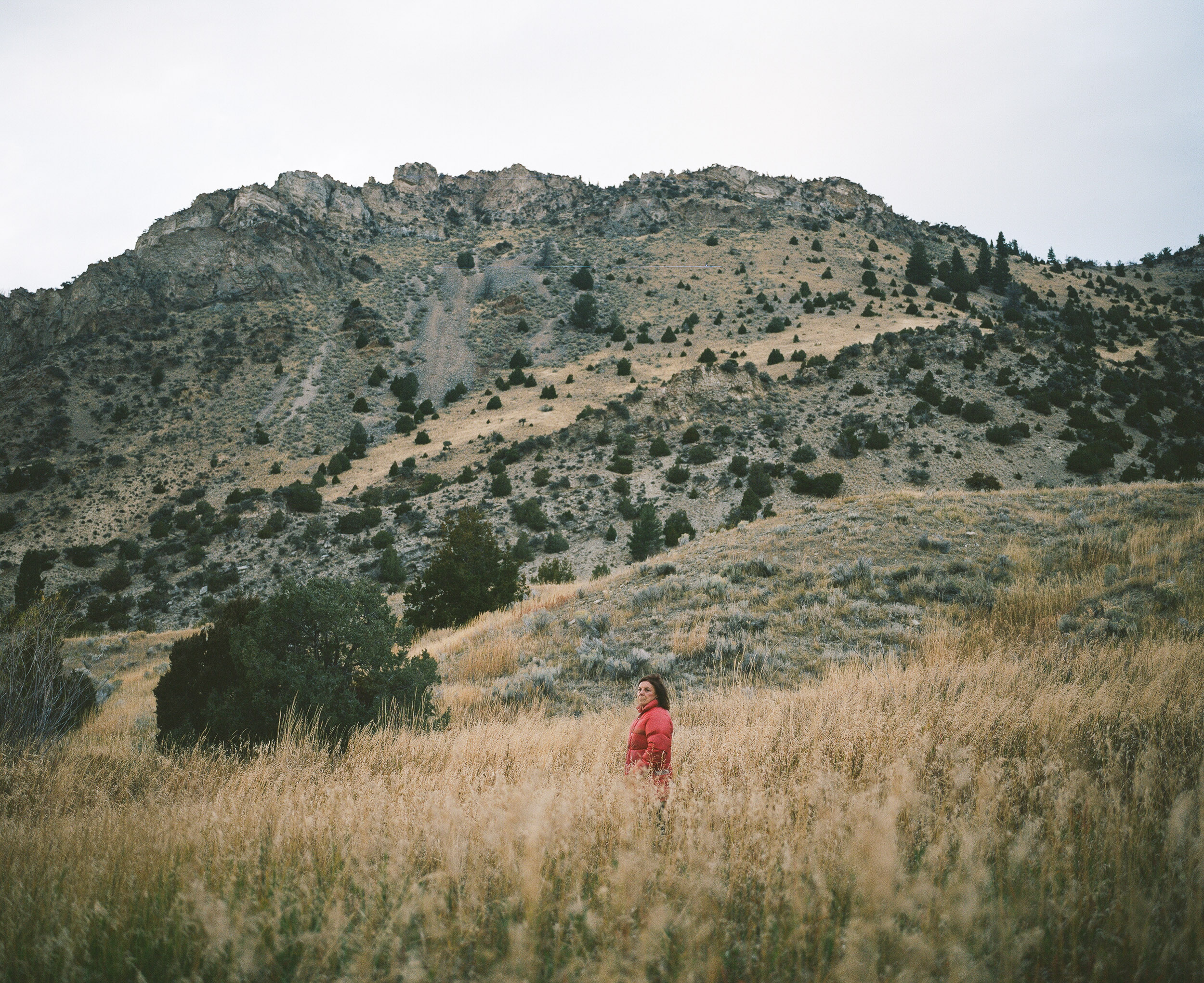 Woman in a red jacket standing in a field with a Mountain behind her.