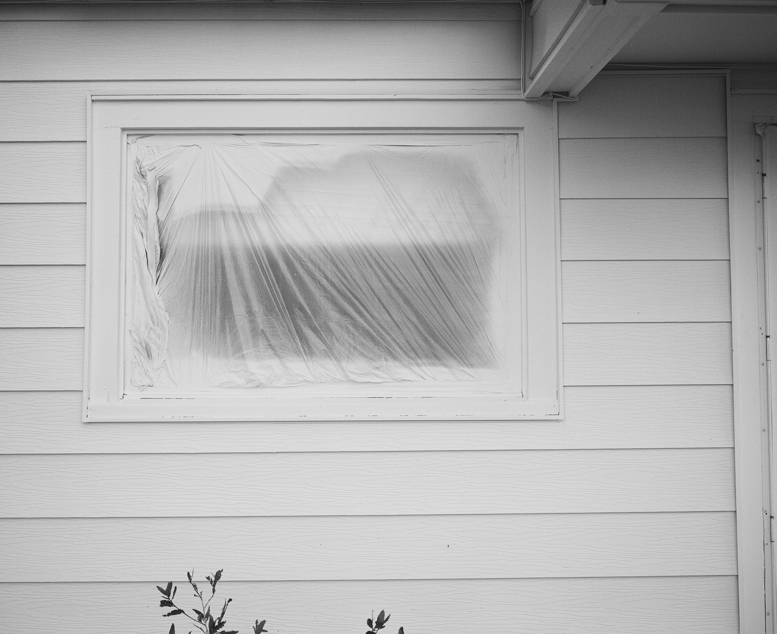 White window covered in plastic on the side of a house