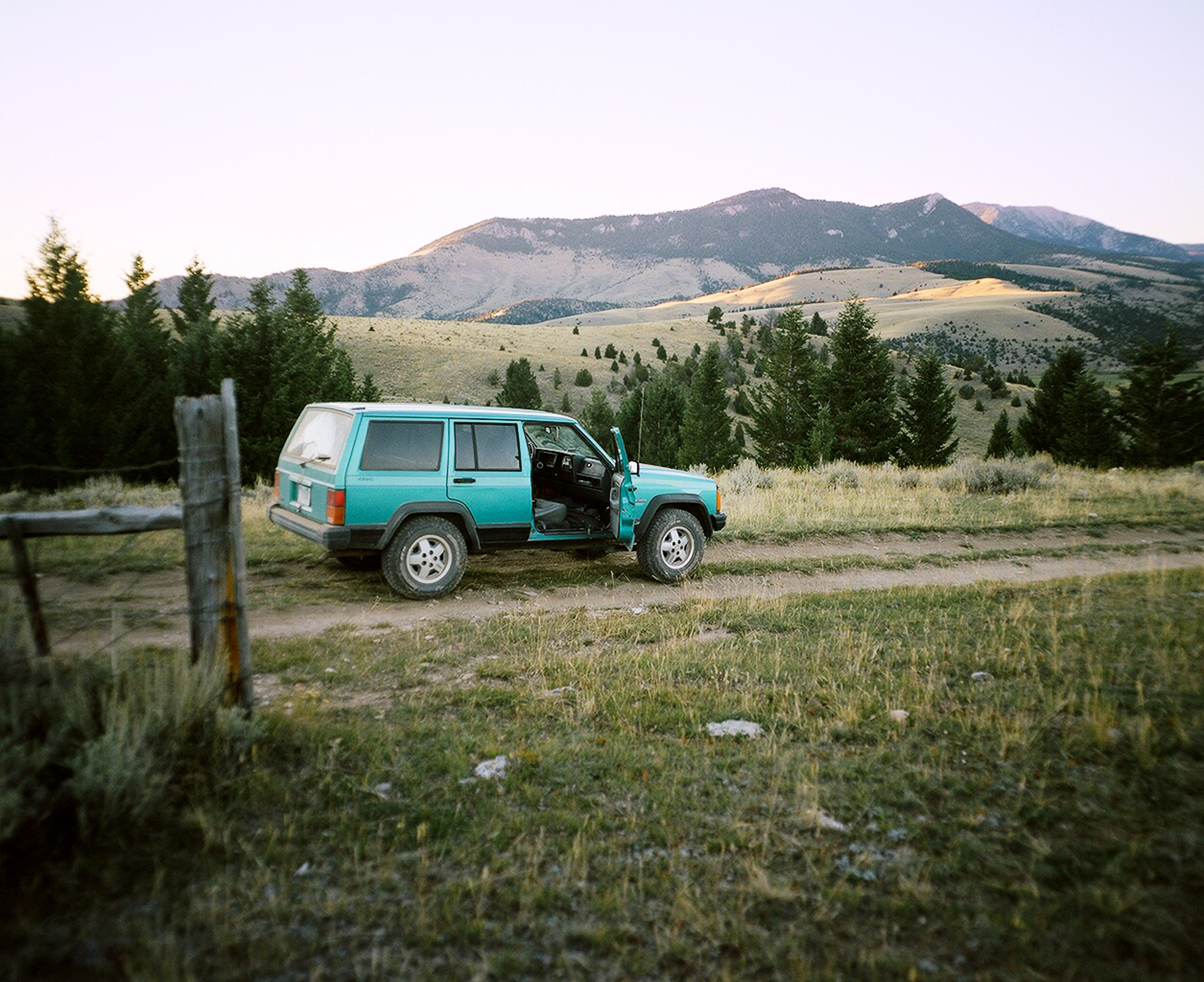 Green Jeep Cherokee with an open passenger door parked on a dirt road in Montana