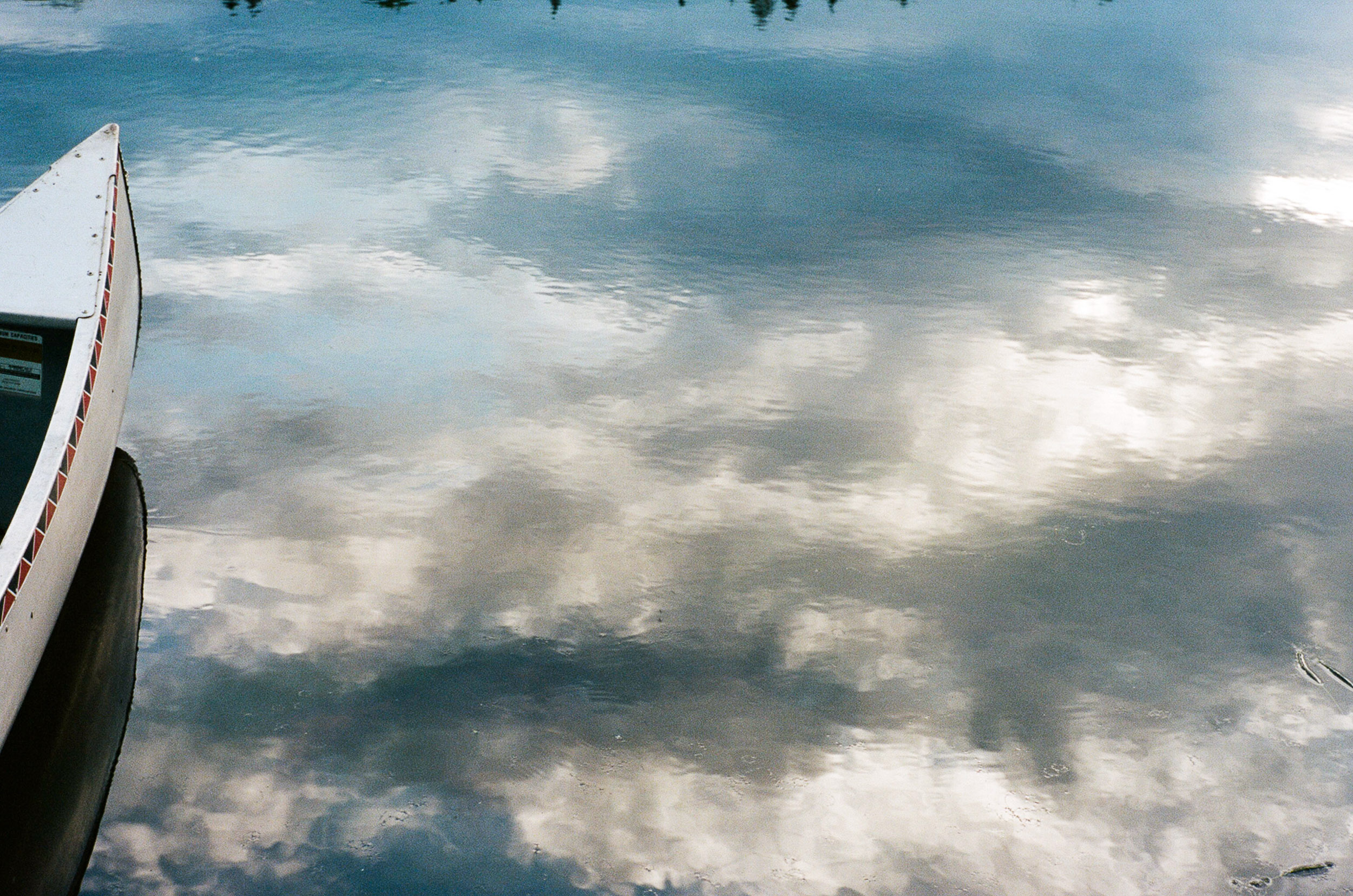 Canoe floating in a lake with cloud reflections