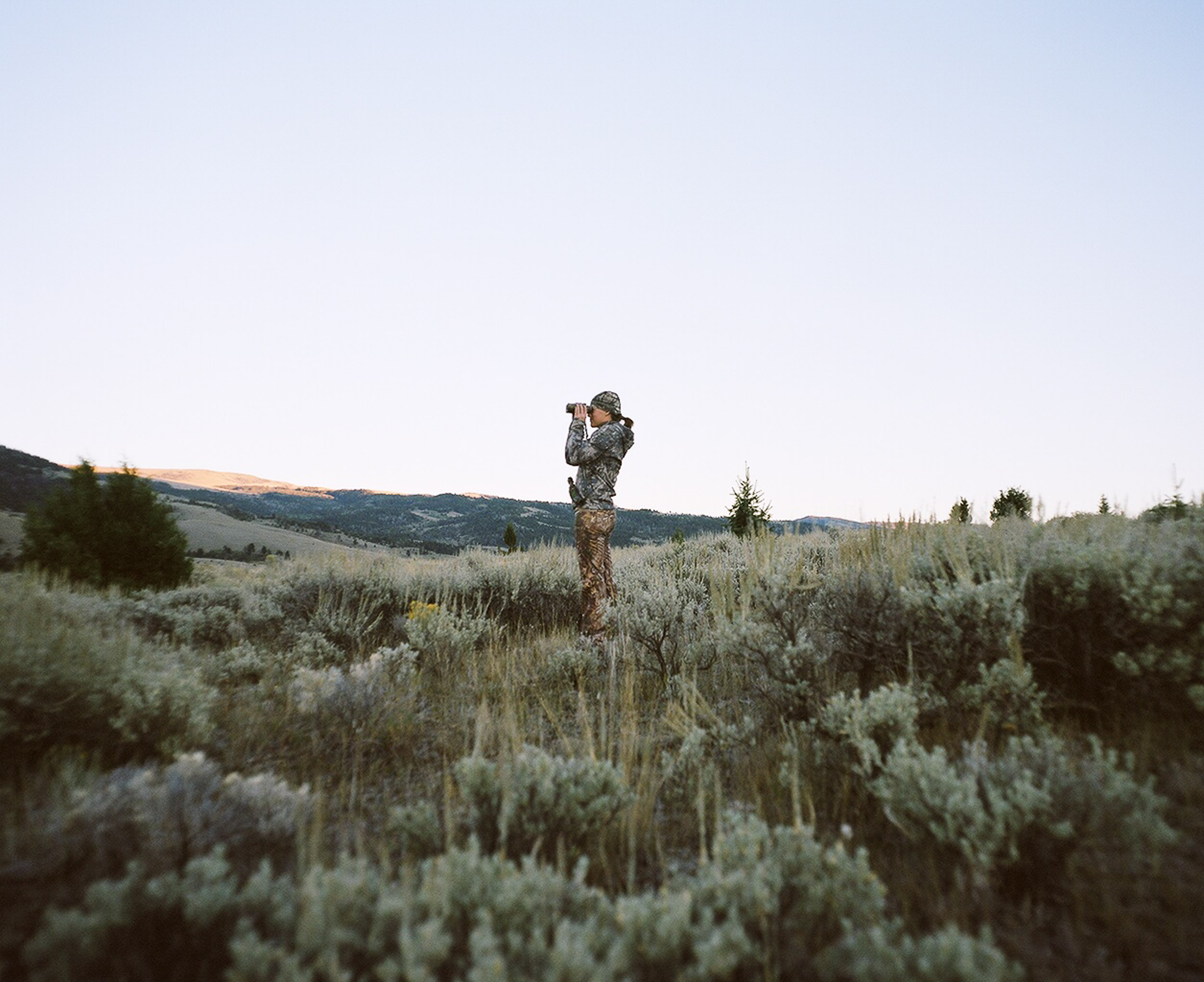 woman hunter looking through binoculars, standing in the sage brush