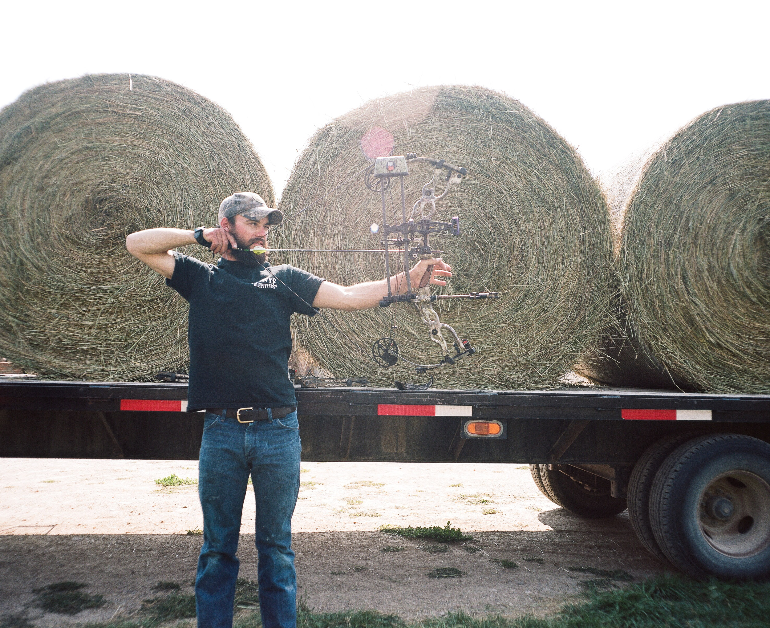 Man shooting a bow in front of bales of hay
