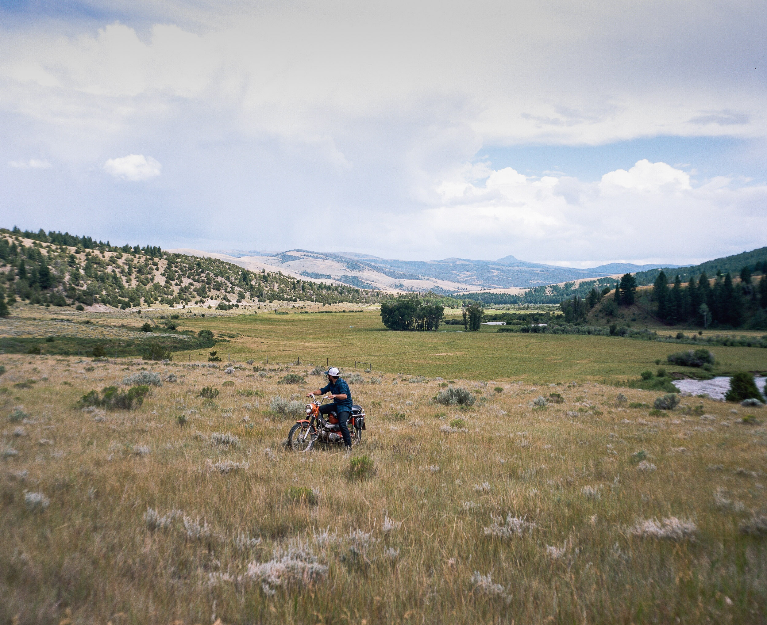 Man on a motorcycle in a field  looking out towards the mountains