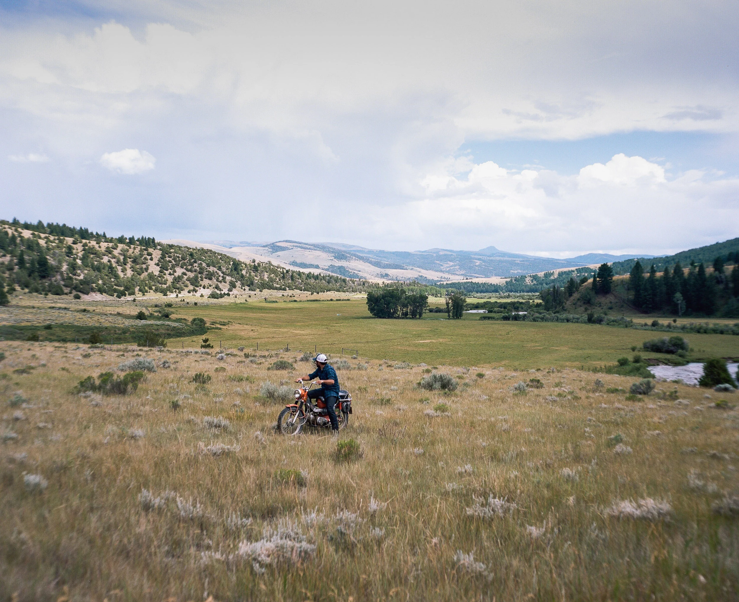 Man on a motorcycle in a field looking out towards the mountains