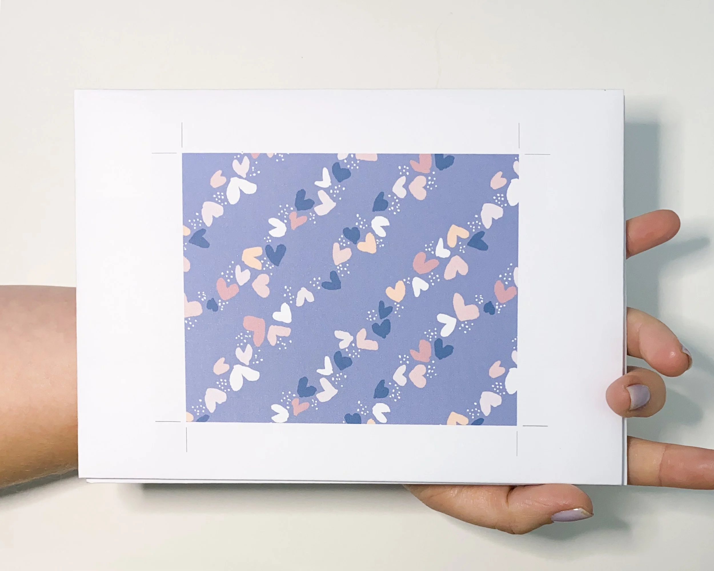 Seamless heart pattern design in pink, white, and navy on blue, printed sample for textile or surface pattern design, held in hand