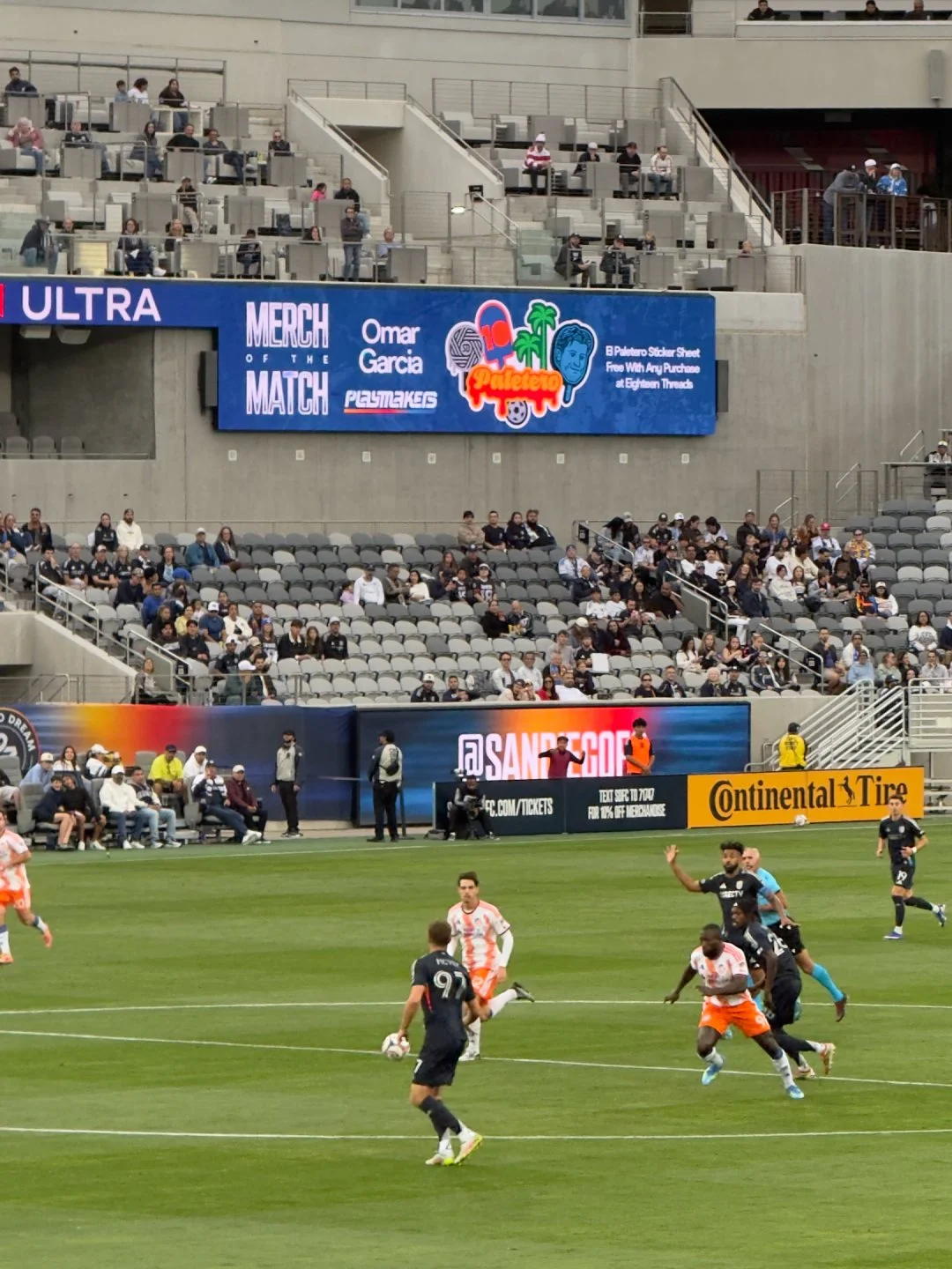Soccer match with players on the field and spectators in the stands, digital advertisements and banners displayed around the stadium.