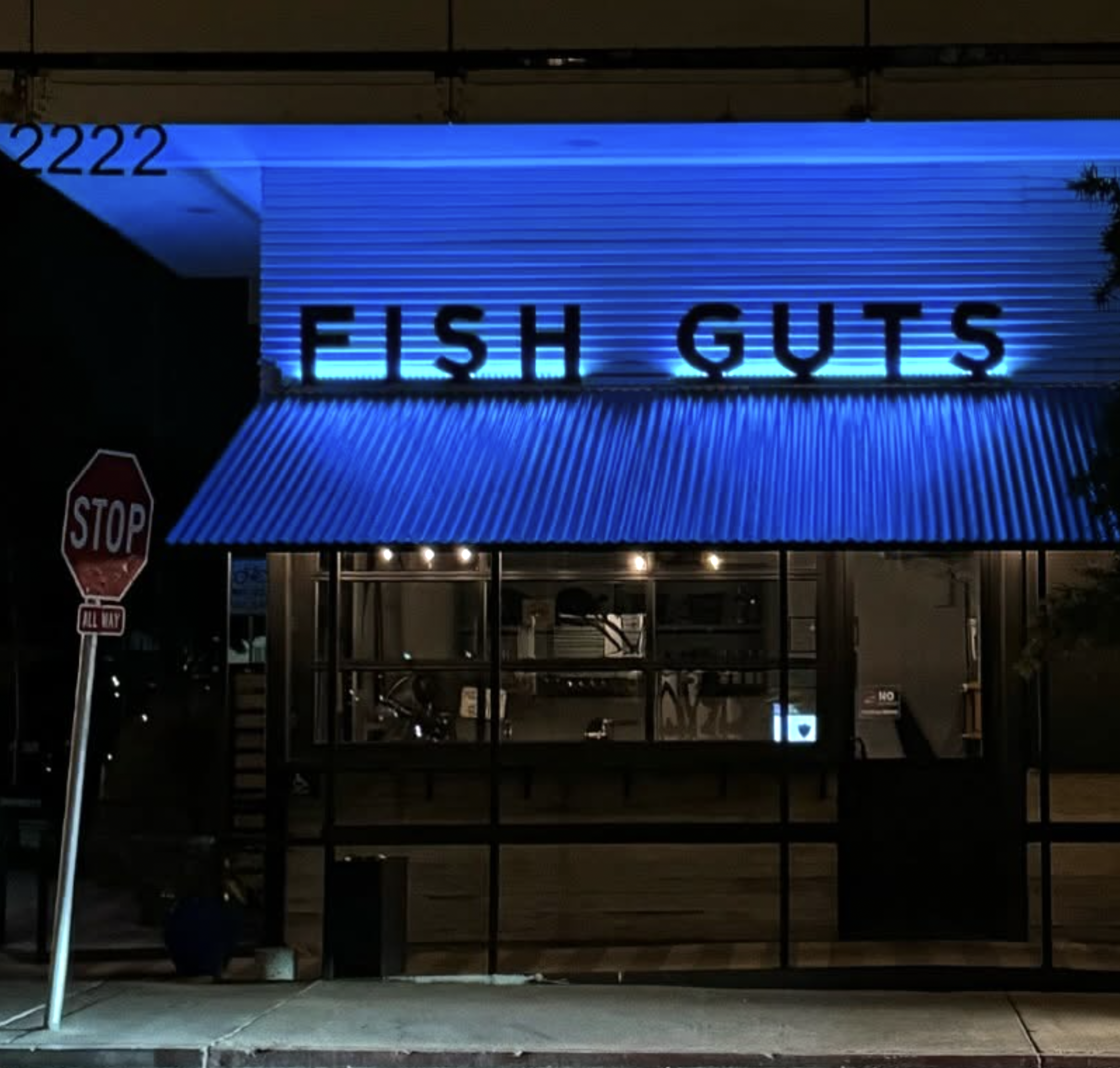 Neon sign reading 'FISH GUTS' in blue lights above a storefront at night.