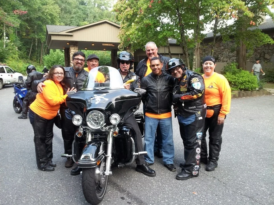 Pastor Tom Hughes sits on his Harley and AMM National President Juan Santos stands to the right wearing a helmet.