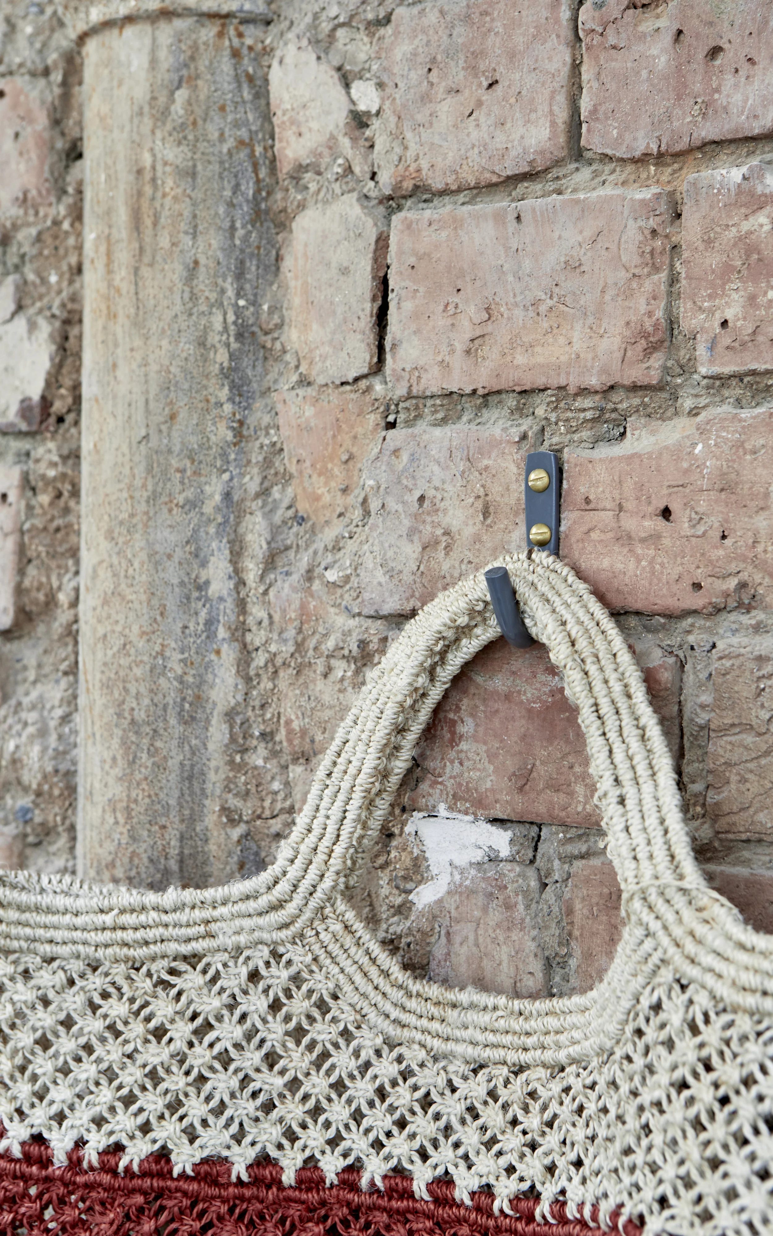 The Grey Hook installed on a red brick wall, showcasing the contrast between industrial metal and rustic texture.