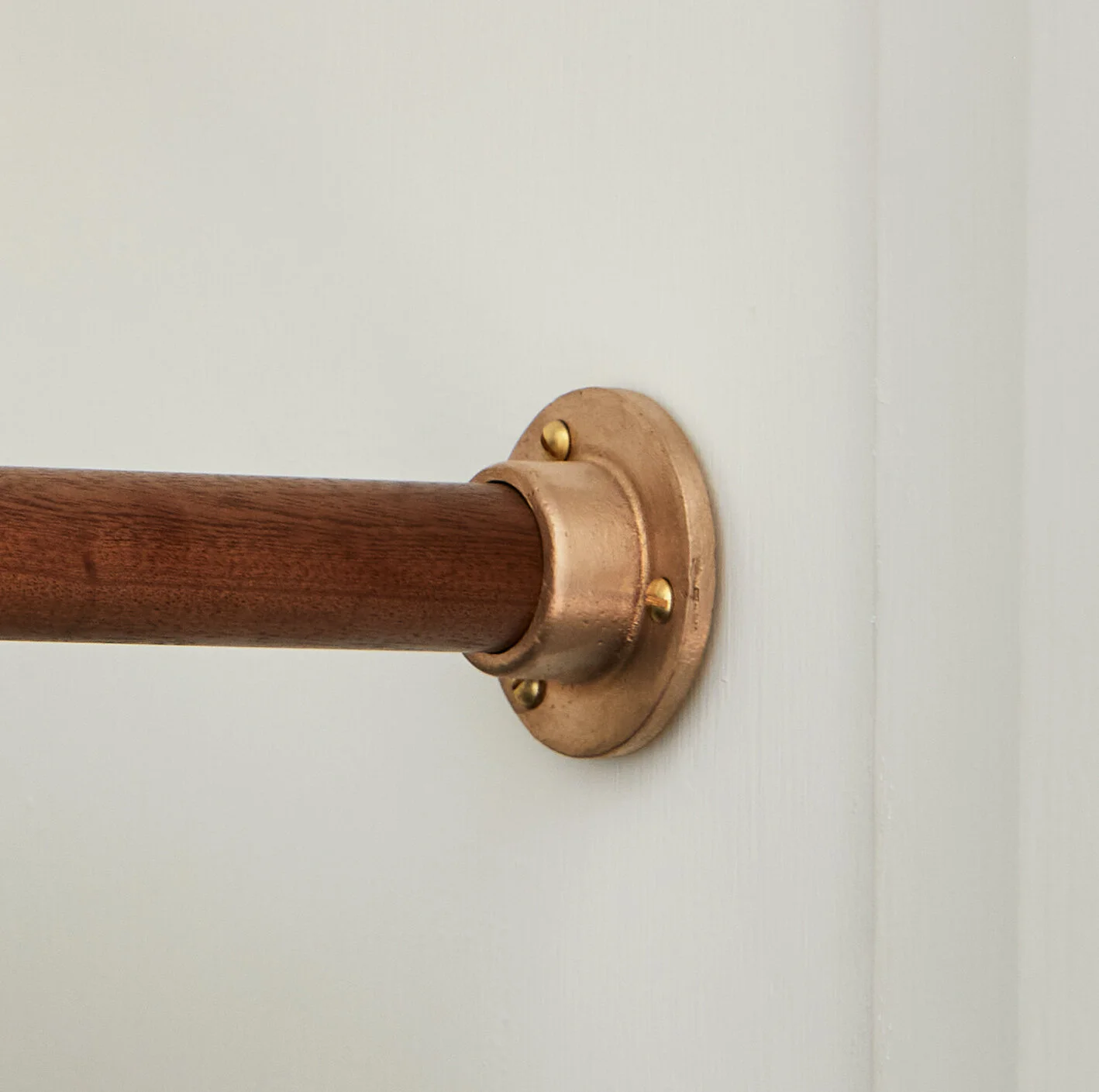 Wardrobe Rail Wall Socket close-up of raw bronze socket and rail fitted to a white wall.