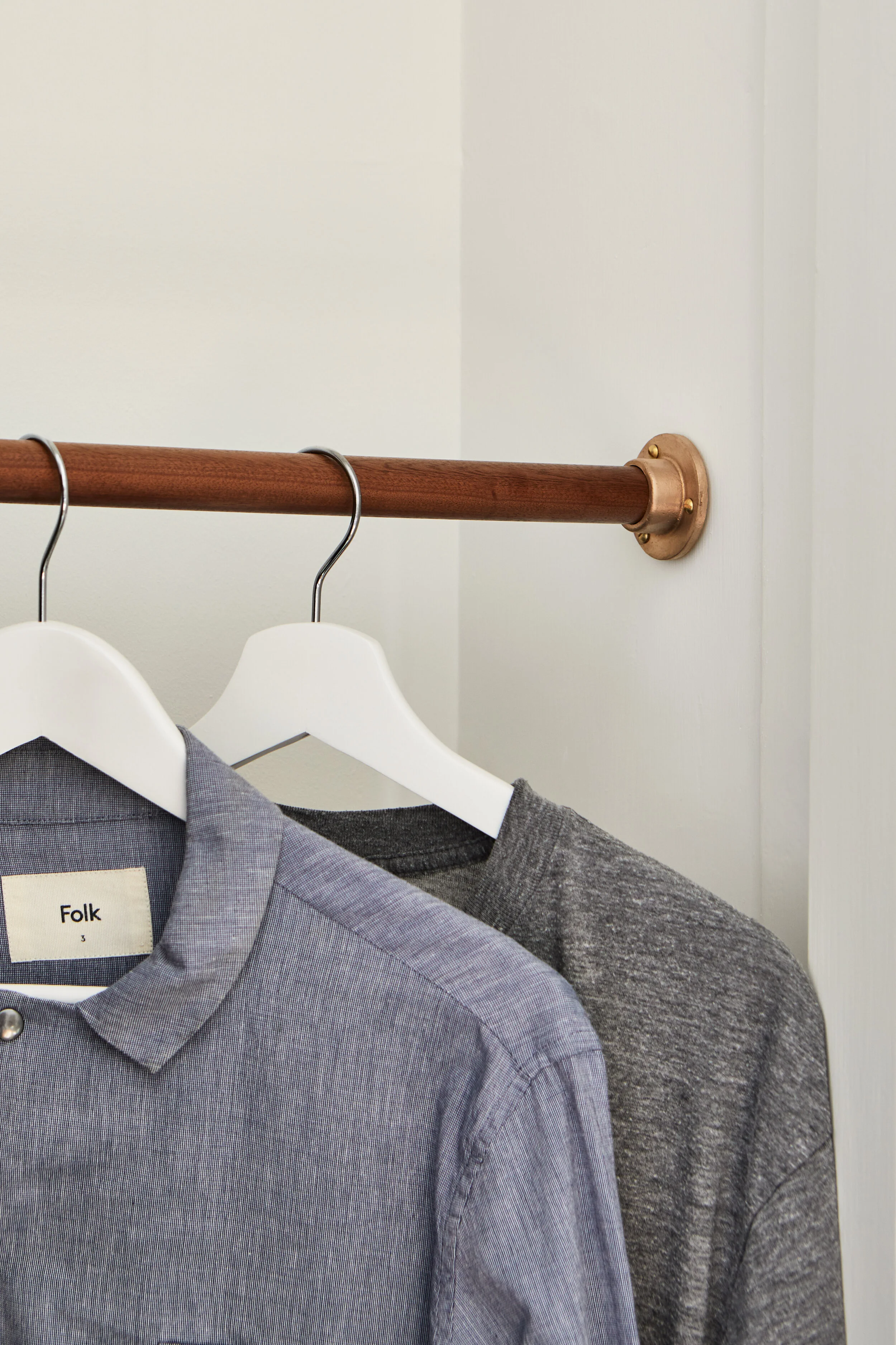 Sapele Hardwood Wardrobe Rail - Close-up view of approximately 30cm of waxed timber rail with two hangers, set in a white painted alcove. Made from sapele hardwood.