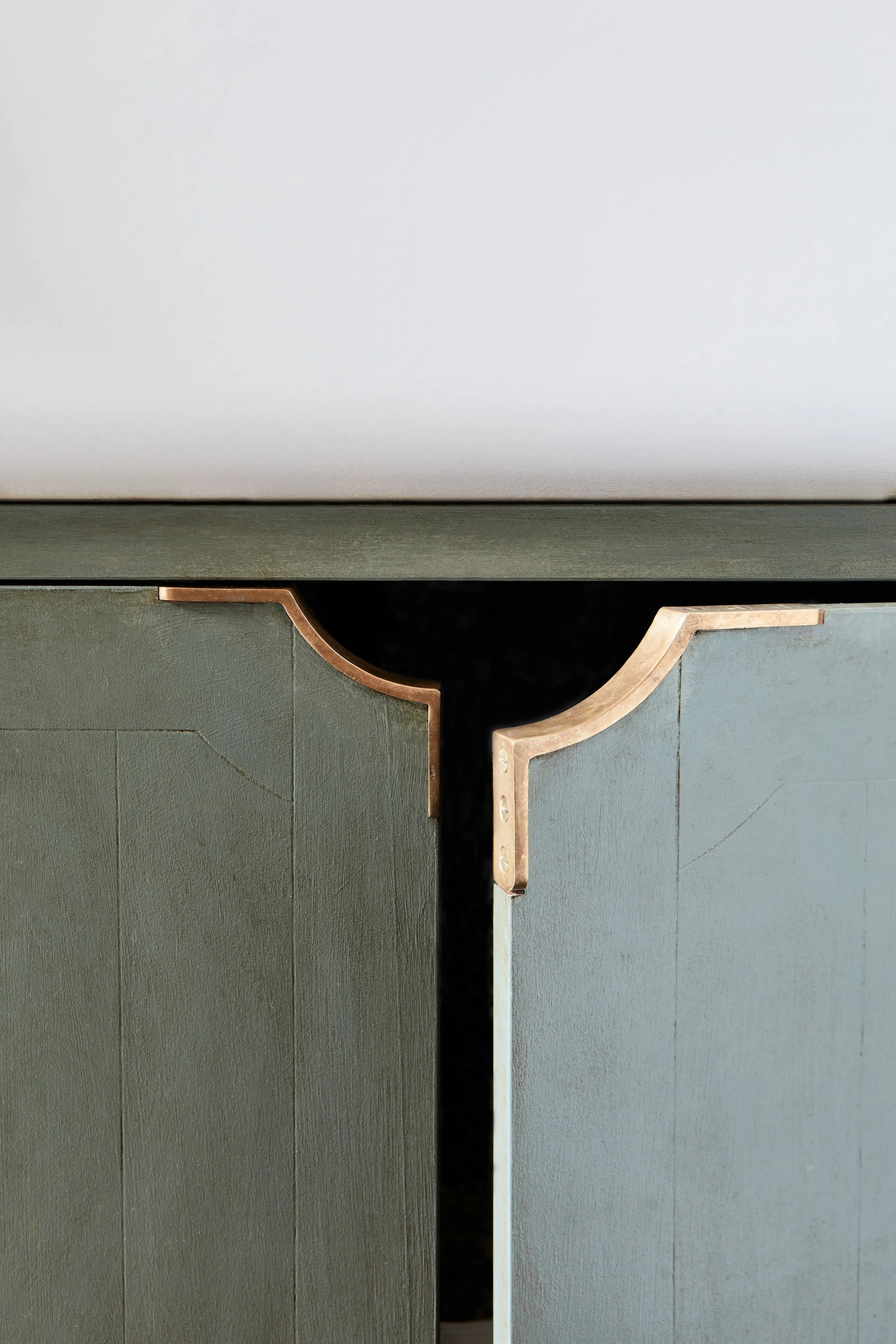Photo of MORAY cupboard pulls on the left and right of a cupboard under the sink, with the right cupboard door ajar, set against door panels hand-painted in an aged green finish.