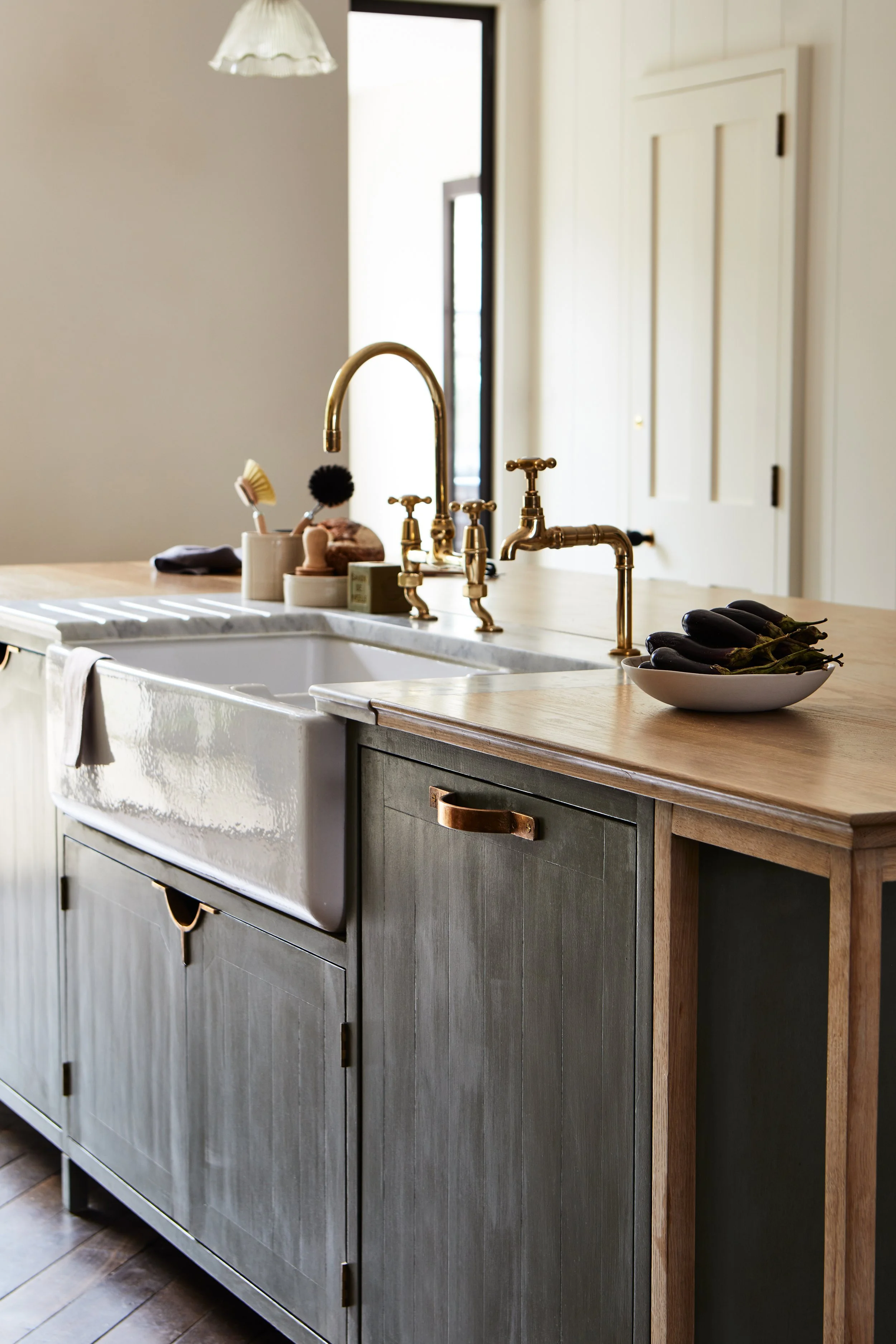 Mid shot of a green hand-painted kitchen island with a Moray kitchen pull on a dishwasher door beside a Belfast sink.